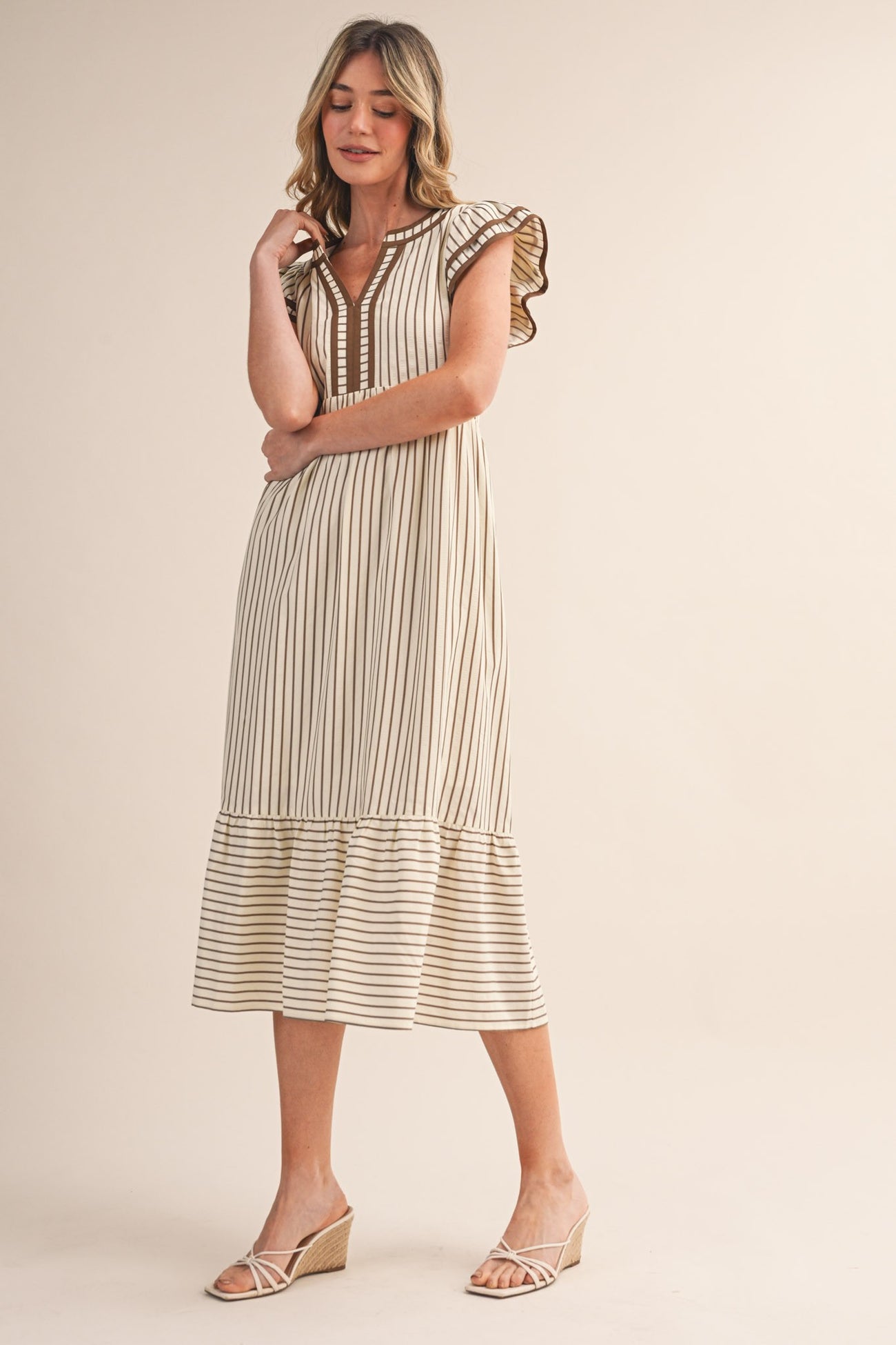woman wearing a cream striped midi dress with ruffled sleeves and a tiered hem, paired with wedge sandals