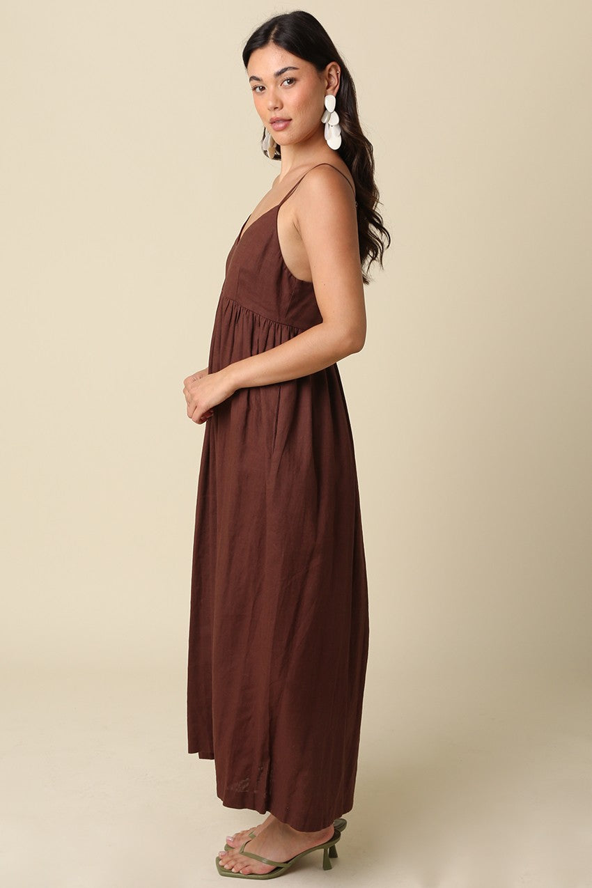 woman wearing a brown maxi dress with a fitted bodice and a flowing skirt, styled with statement earrings and strappy sandals