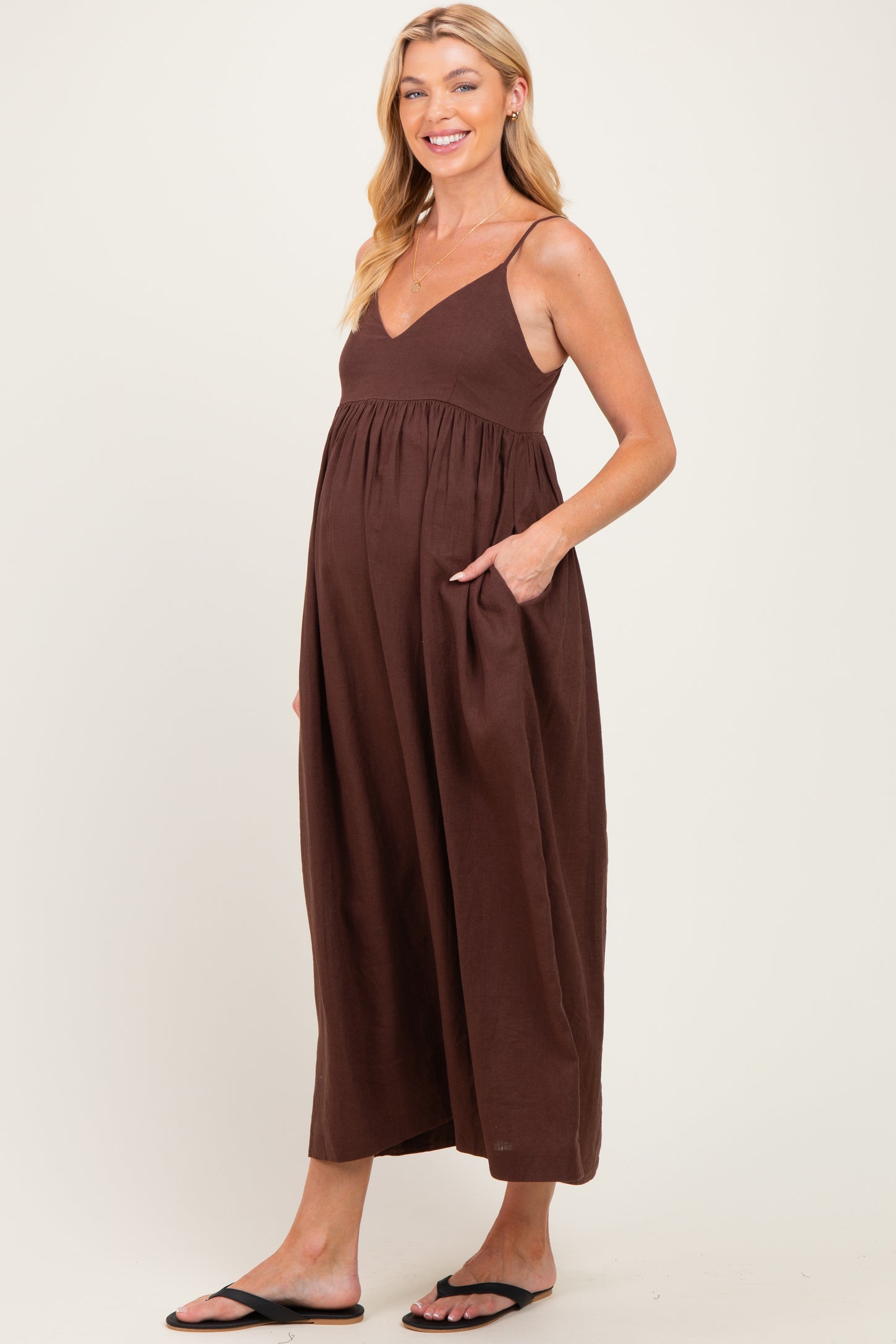 woman wearing a chocolate brown maternity maxi dress with a v-neckline and pockets, showing her baby bump