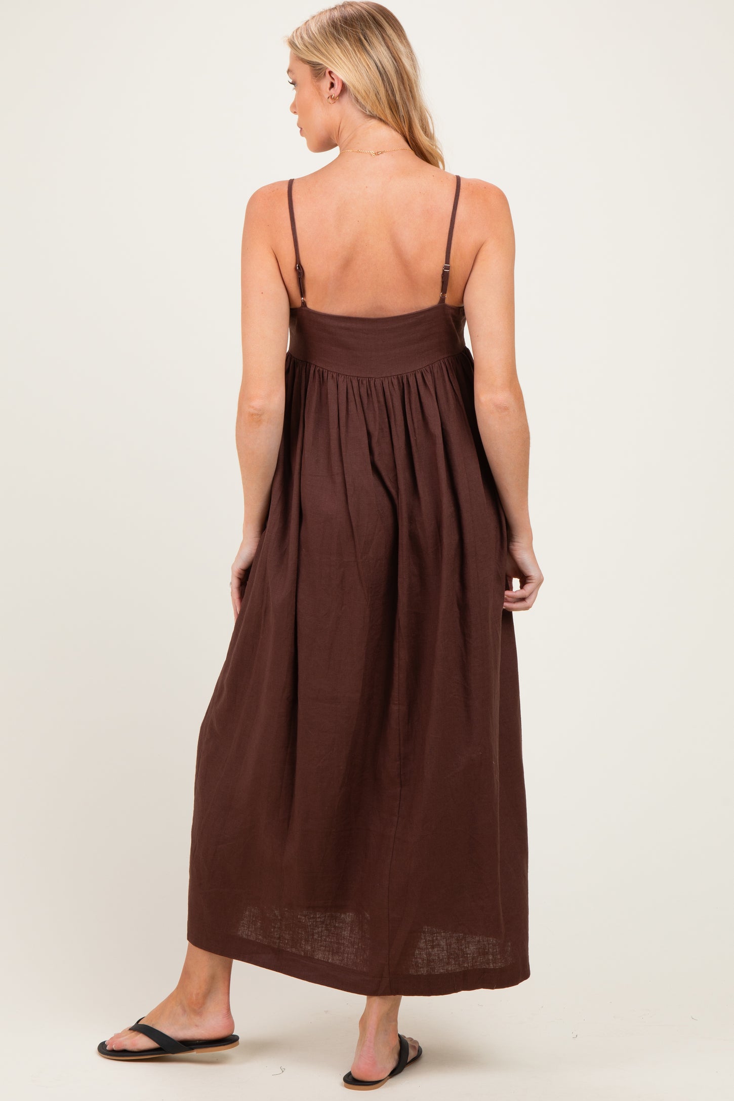 woman wearing a brown maternity maxi dress with adjustable spaghetti straps and a flowy skirt from the back