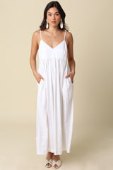 woman wearing a white maxi dress with spaghetti straps and pockets, styled with statement earrings