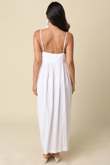 woman wearing a white backless maxi dress with thin straps and a gathered waist, standing against a neutral background