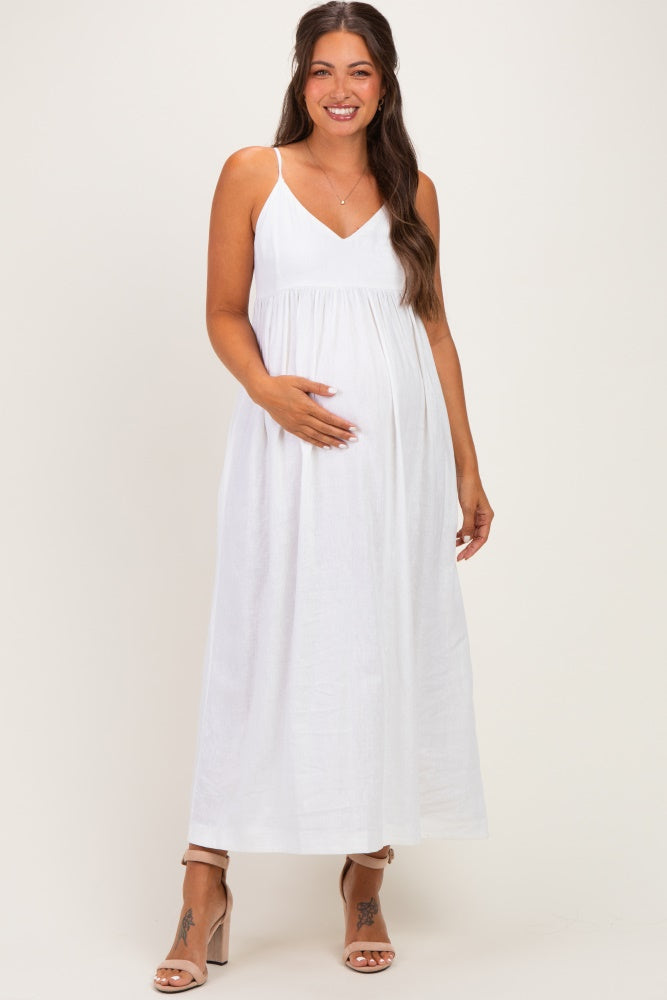 woman wearing a white maternity maxi dress with spaghetti straps and holding her baby bump