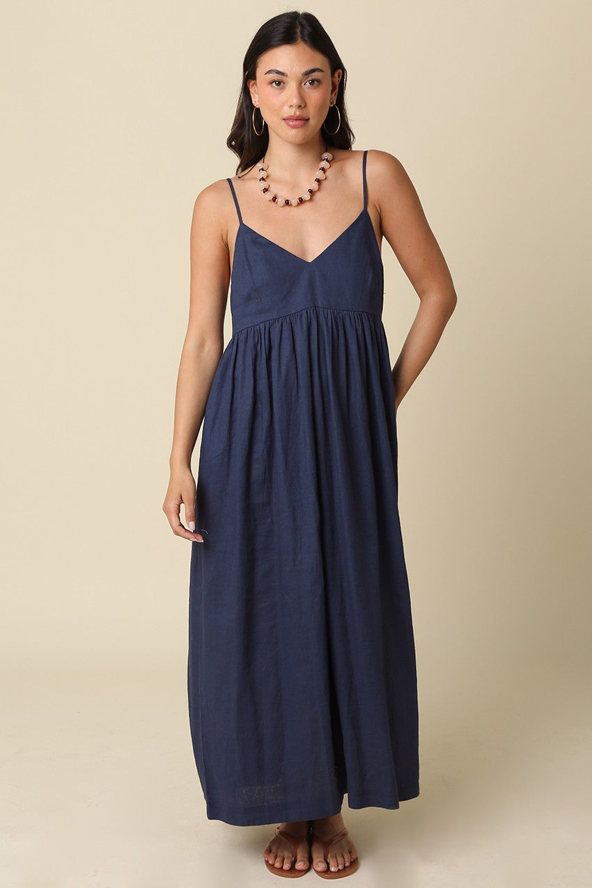 woman wearing a navy blue maxi dress with a v-neckline and thin straps, standing against a beige background