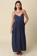 woman wearing a navy blue maxi dress with a v-neckline and thin straps, standing against a beige background