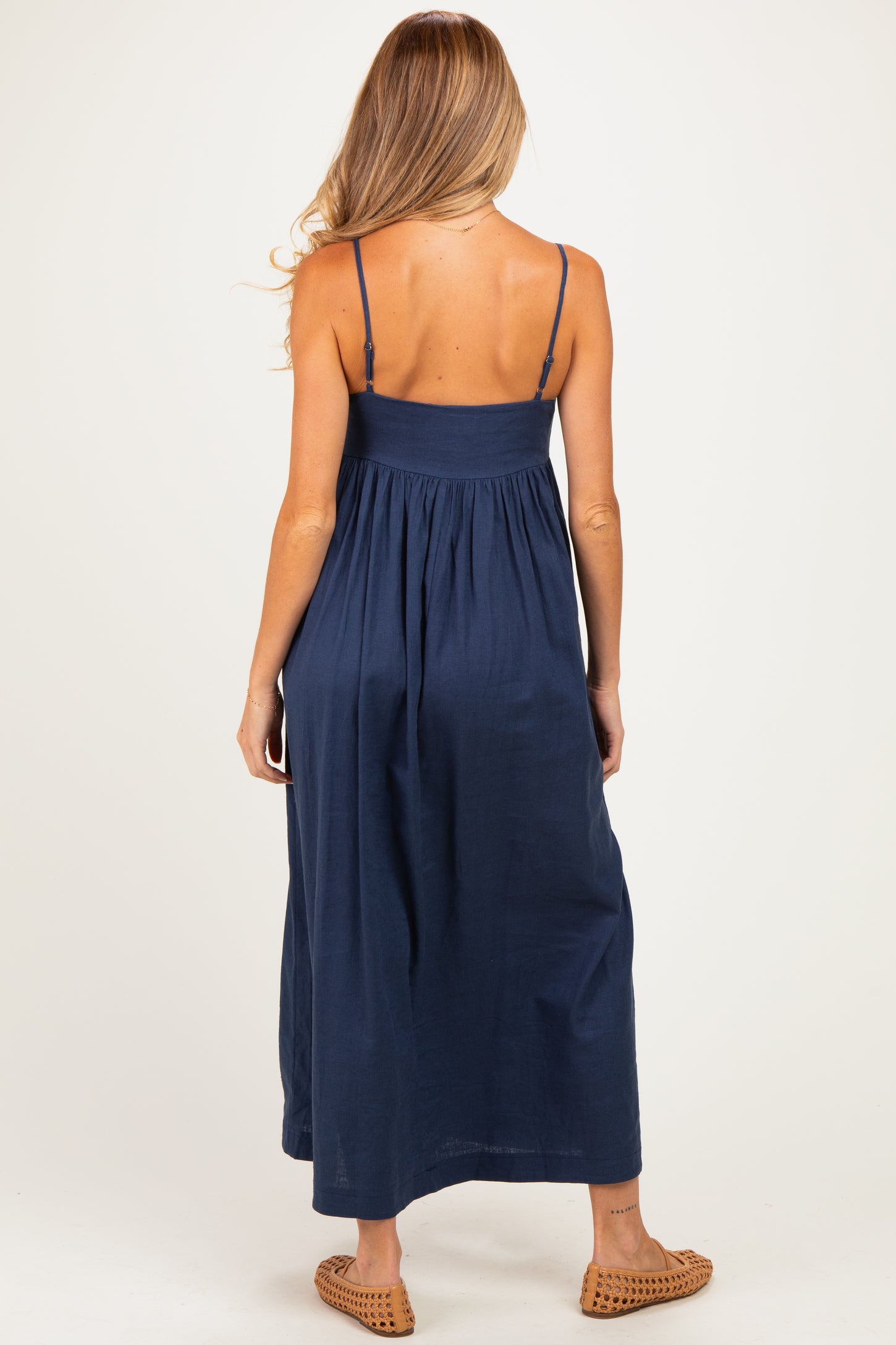 woman wearing a navy blue maternity maxi dress with adjustable straps and a flowy silhouette, showing a baby bump on the back