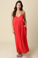 woman wearing a red maxi dress with spaghetti straps and a flowy skirt, standing against a neutral background