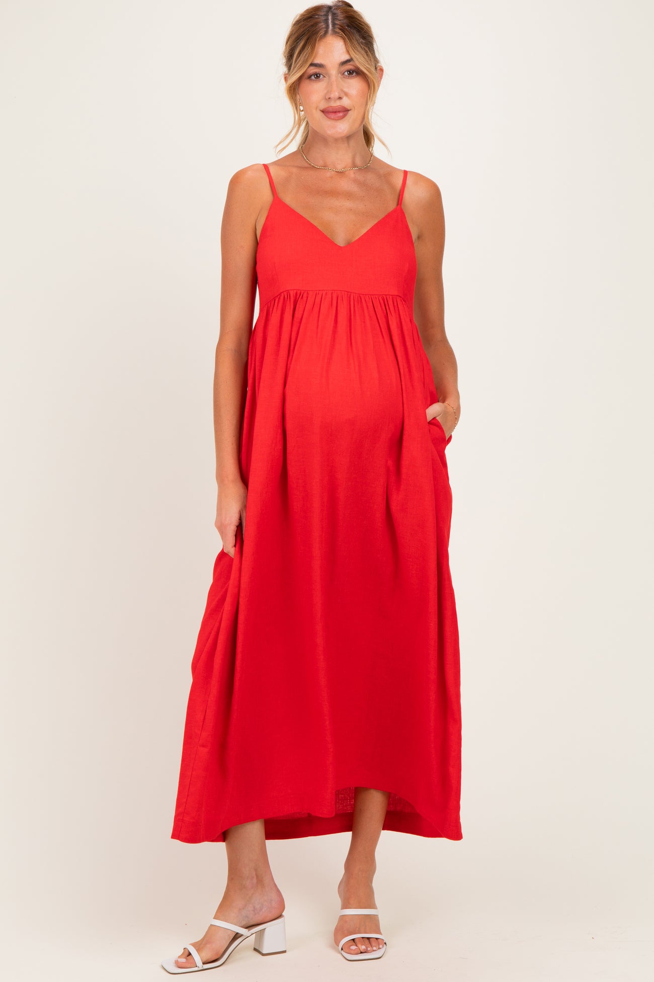 woman wearing a red maternity maxi dress with a v-neckline and pockets, showcasing her baby bump