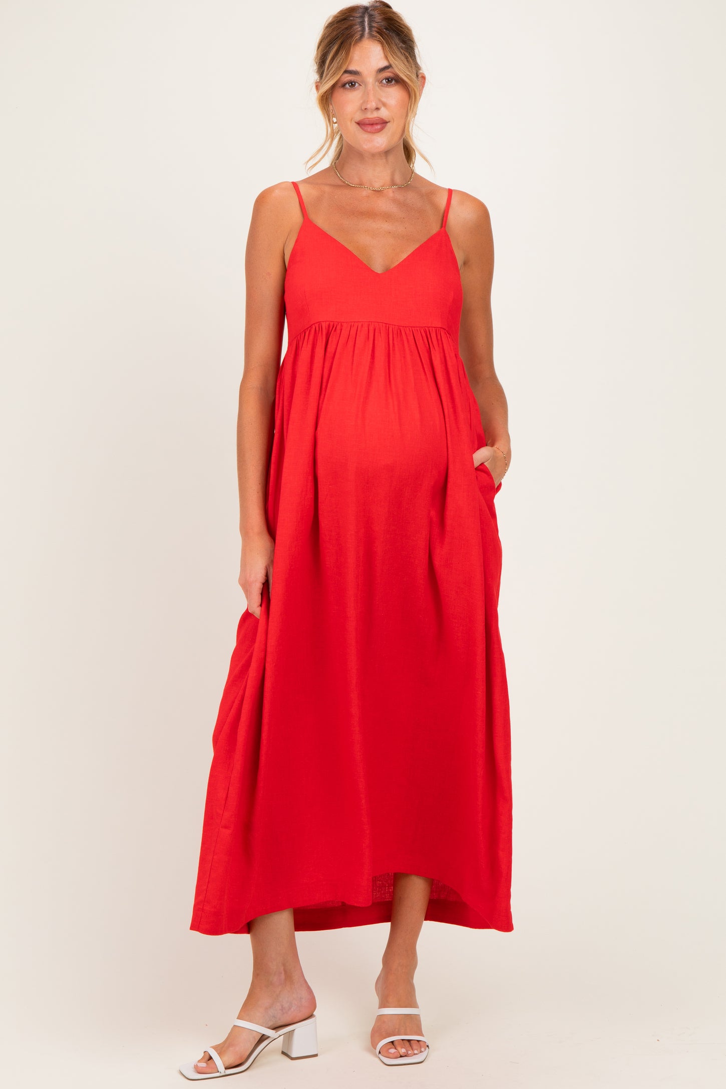 woman wearing a red maternity maxi dress with a v-neckline and pockets, showcasing her baby bump