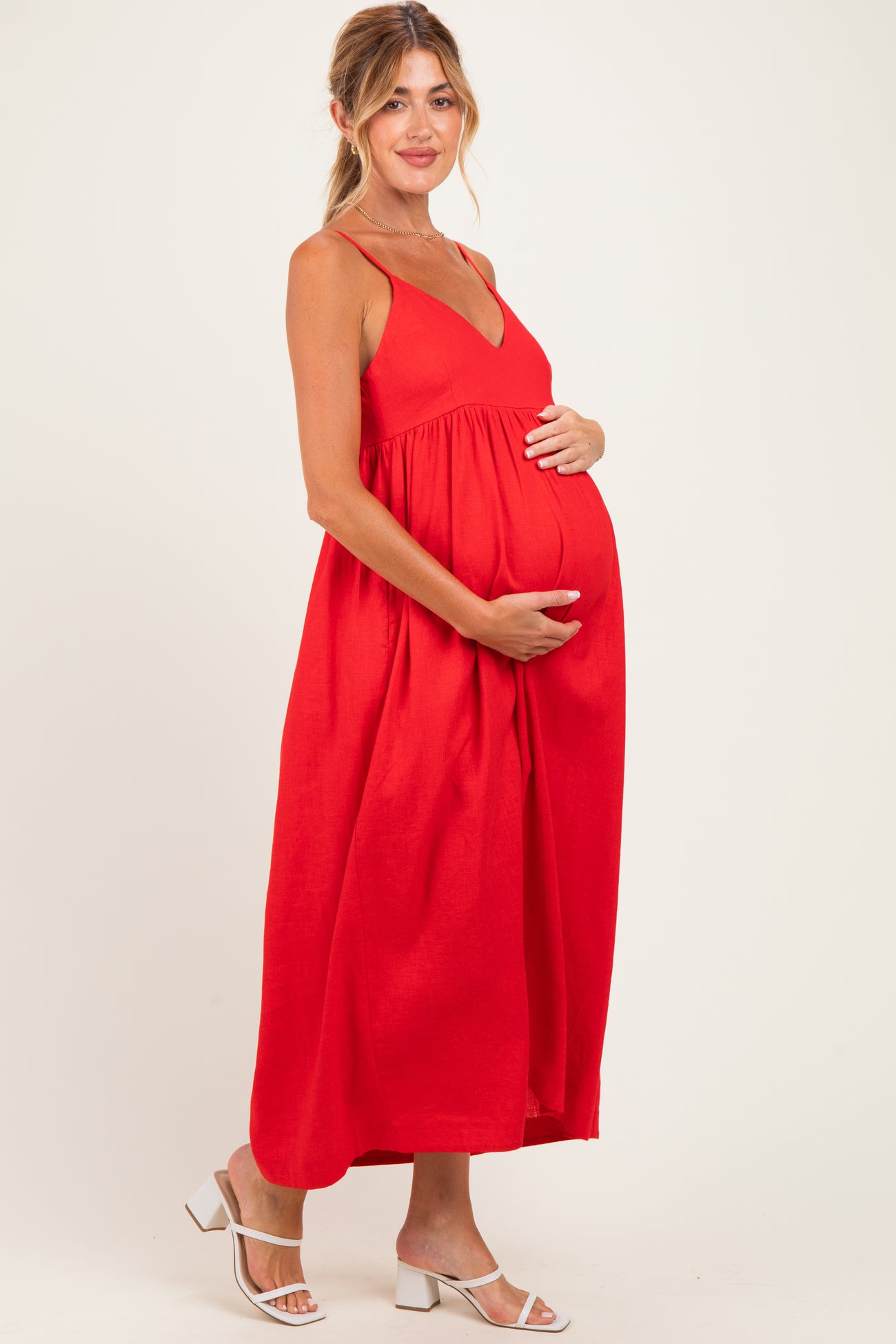 woman wearing a red maternity maxi dress with a v-neckline and holding her baby bump