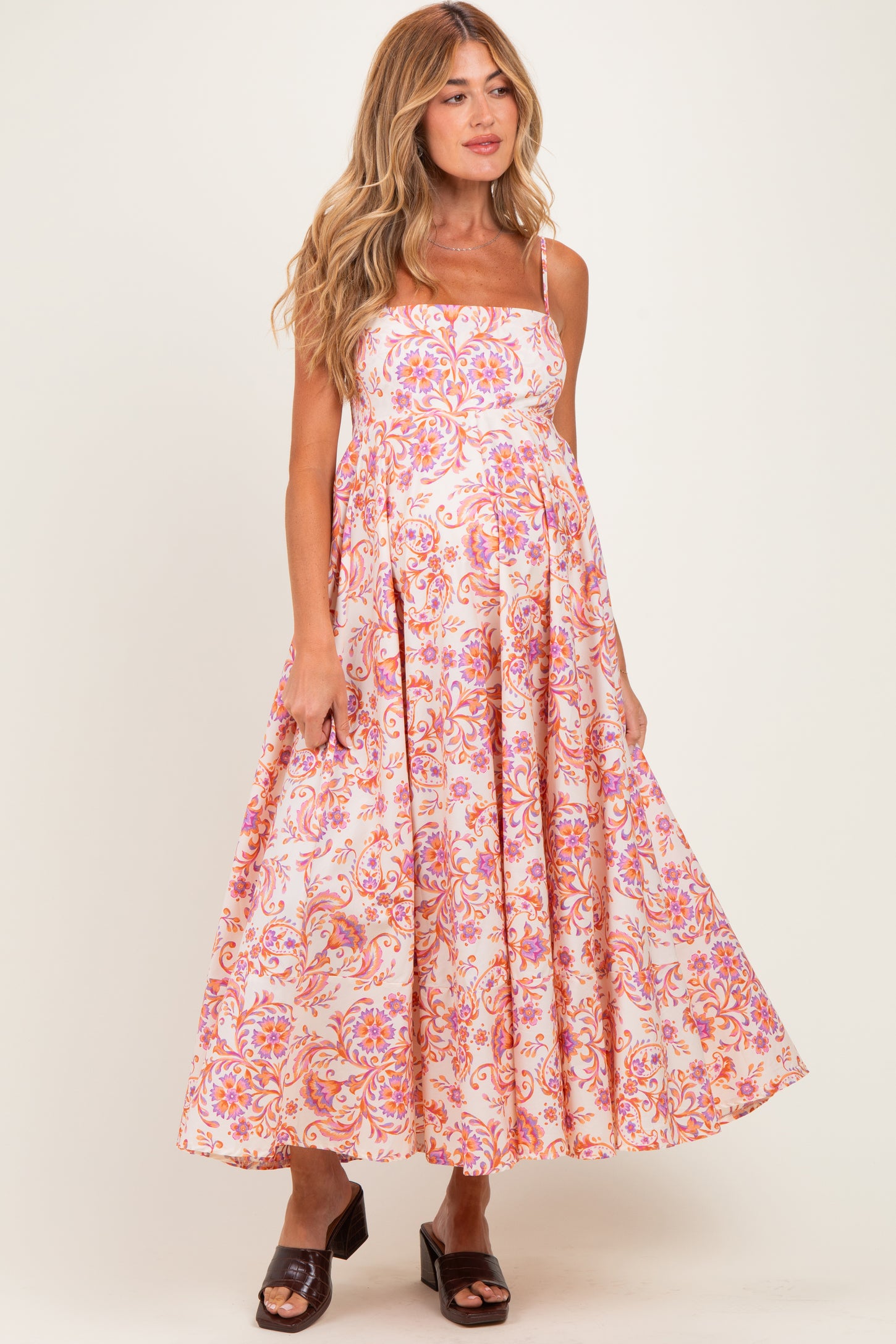 woman wearing a pink and white floral maternity dress with spaghetti straps and a flowy skirt, showing her baby bump