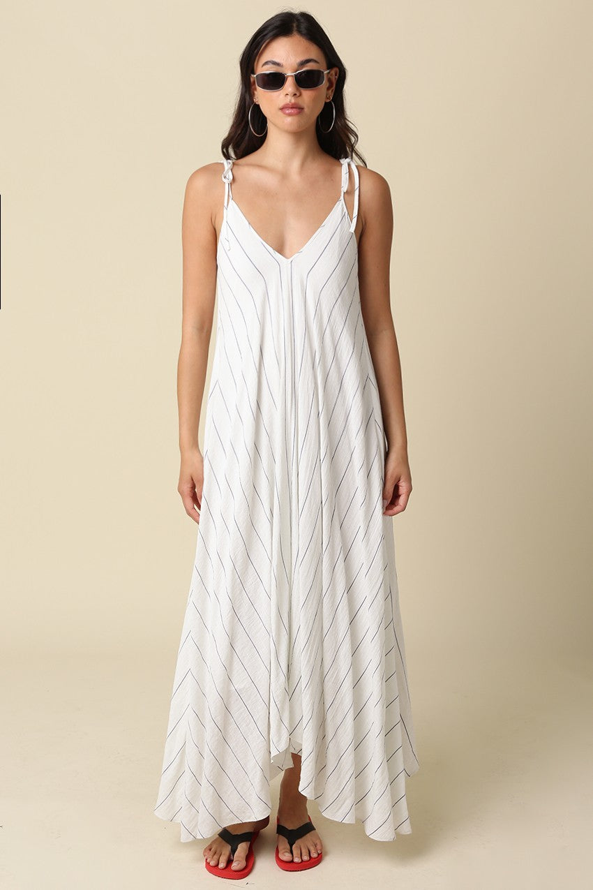 woman wearing a white striped maxi dress with adjustable straps and a flowy silhouette, paired with sunglasses and flip-flops