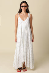 woman wearing a white striped maxi dress with adjustable straps and a flowy silhouette, paired with sunglasses and flip-flops