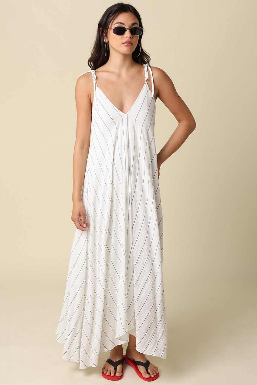 woman wearing a white striped maxi dress with adjustable straps and a flowing silhouette, paired with sunglasses and flip flops