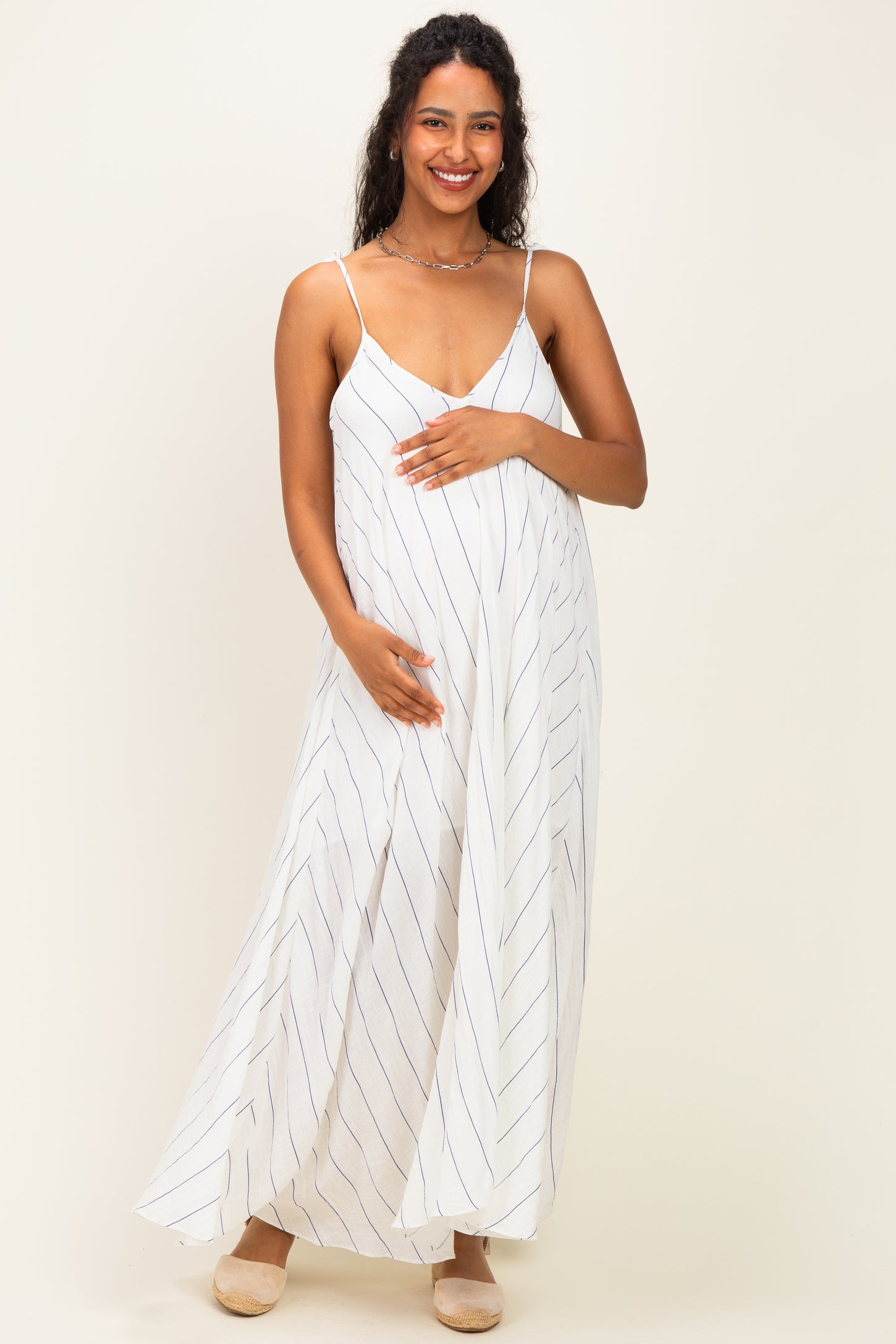 woman wearing a white striped maternity maxi dress and gently holding her baby bump
