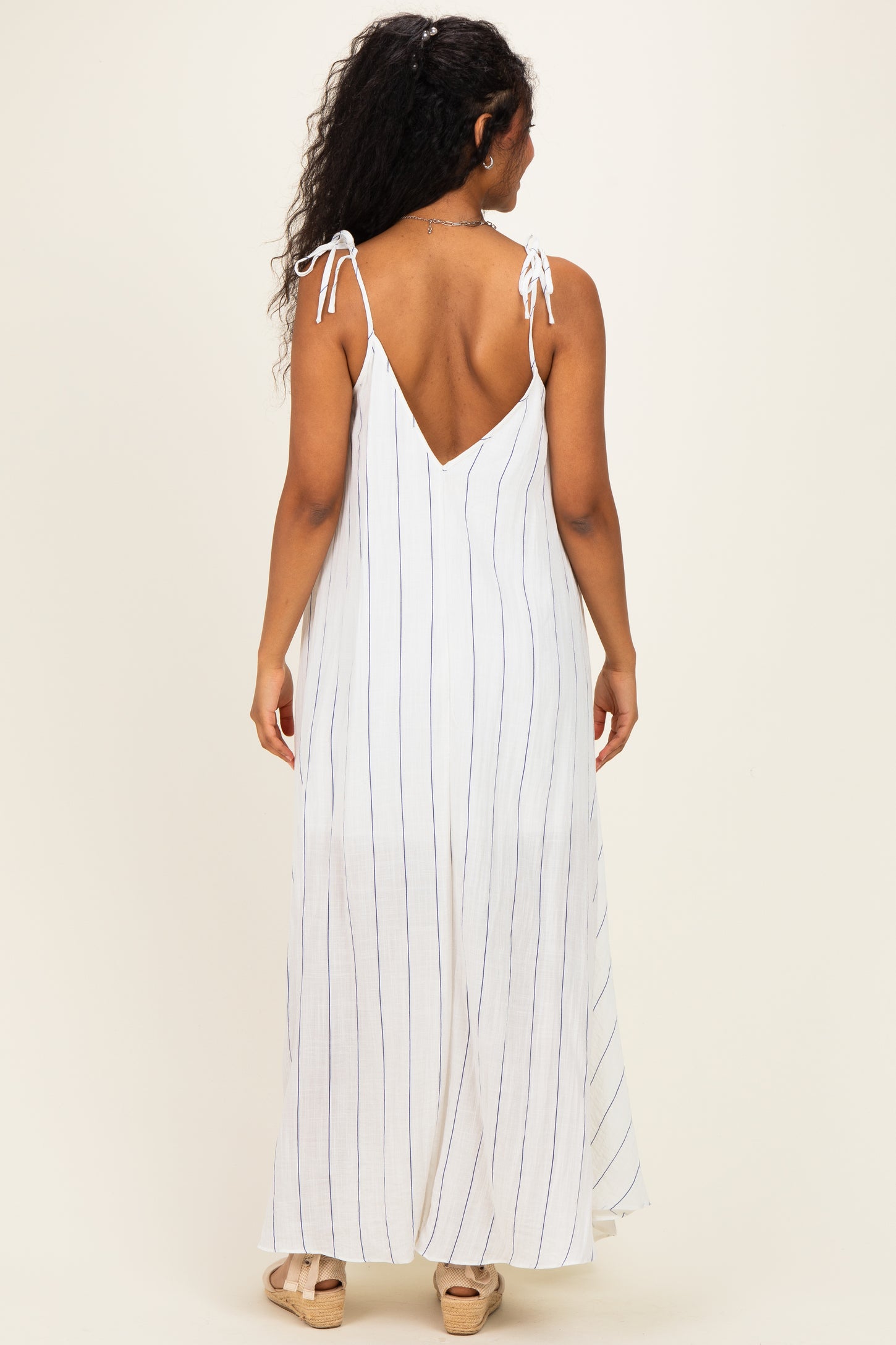 woman wearing a white and blue striped maternity maxi dress with tie straps and a low back