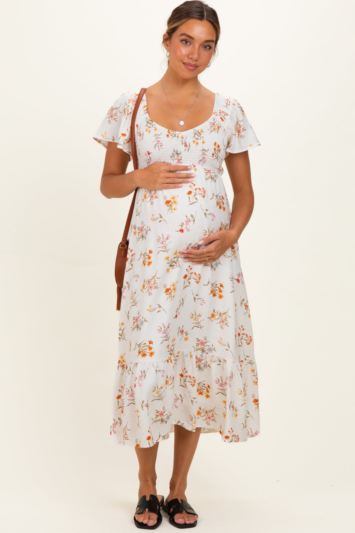 woman wearing a white floral maternity dress with short sleeves and a baby bump, holding her belly