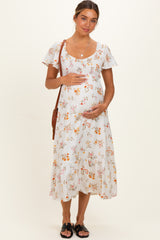 woman wearing a white floral maternity dress with short sleeves and a baby bump, holding her belly
