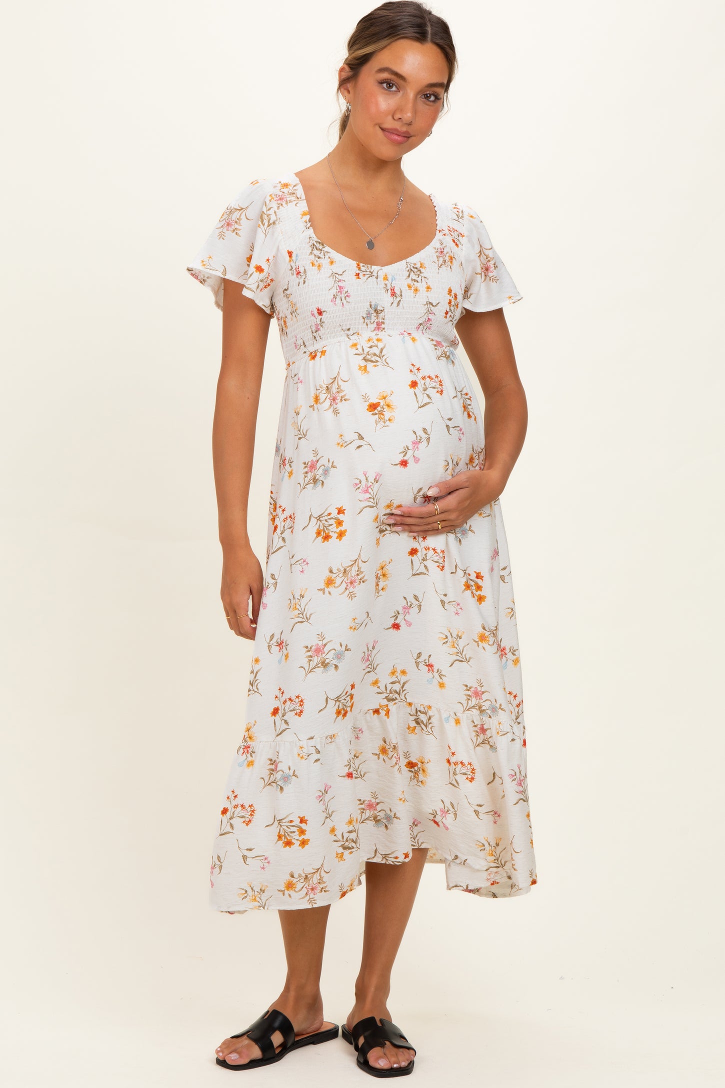 woman wearing a floral maternity dress with short ruffled sleeves and holding her baby bump
