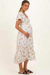 woman wearing a white floral maternity dress with short sleeves and a gathered waist, holding her baby bump
