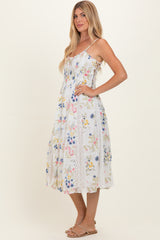 woman wearing a white floral maxi dress with lace detailing and thin straps, standing sideways during a photoshoot