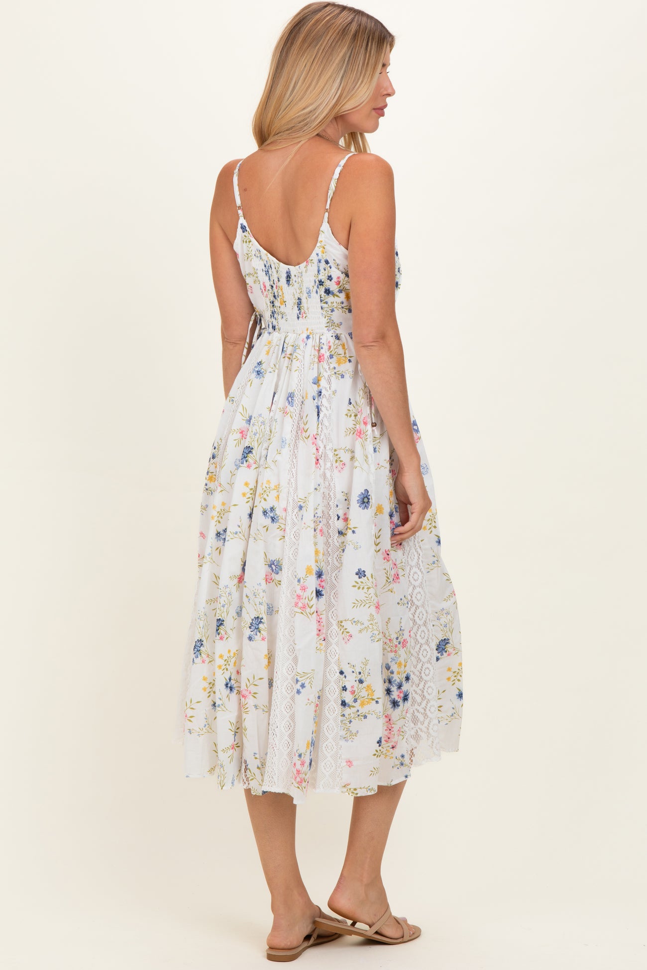 woman wearing a white floral maxi dress with a lace hem and spaghetti straps, viewed from the back