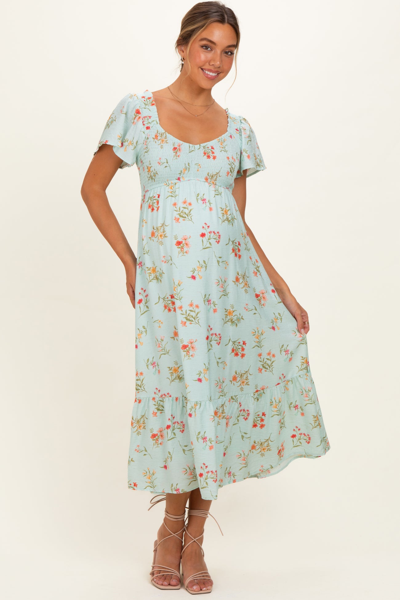 woman wearing a light blue floral maternity dress with short sleeves and a smocked bodice, showcasing her baby bump