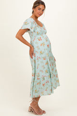 woman wearing a light blue floral maternity dress, showing her baby bump, with a tiered skirt and short sleeves