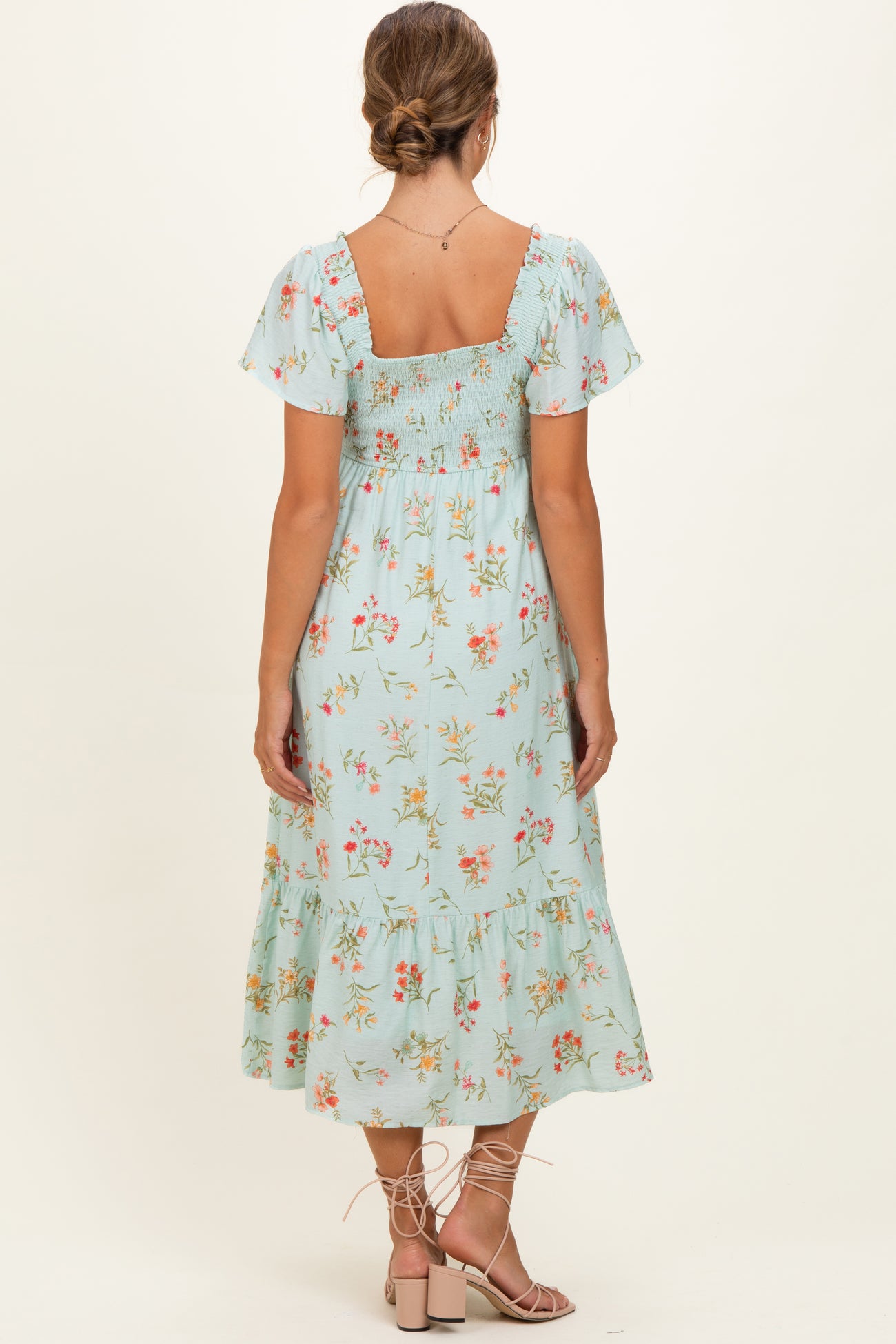 woman wearing a mint green floral maternity dress with short sleeves and a ruffled hem, showing a baby bump from the back