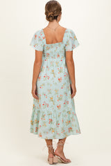 woman wearing a mint green floral maternity dress with short sleeves and a ruffled hem, showing a baby bump from the back