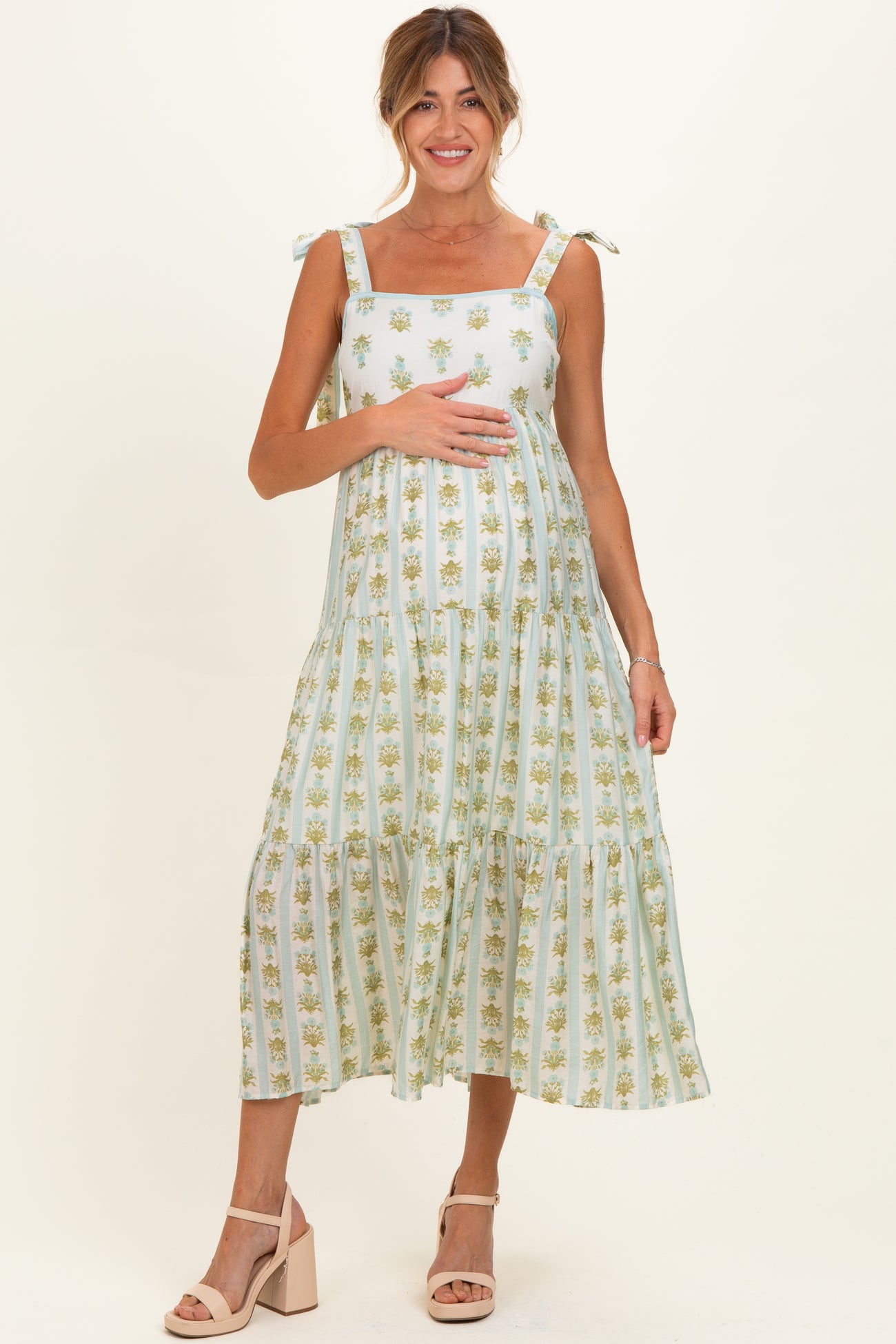 woman wearing a light green floral maternity dress with tie straps and holding her baby bump