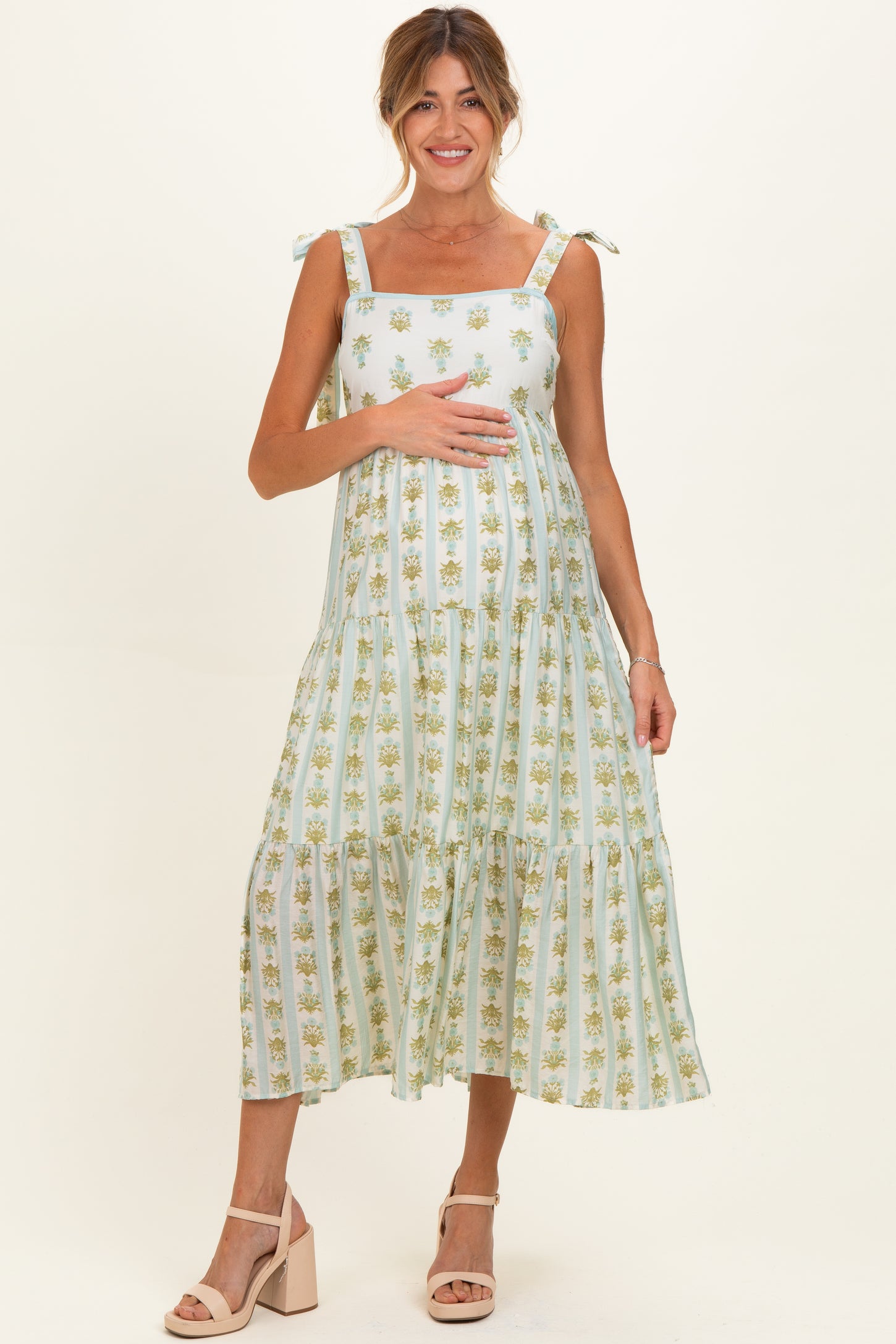 woman wearing a light green floral maternity dress with tie straps and holding her baby bump