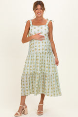 woman wearing a light green floral maternity dress with tie straps and holding her baby bump