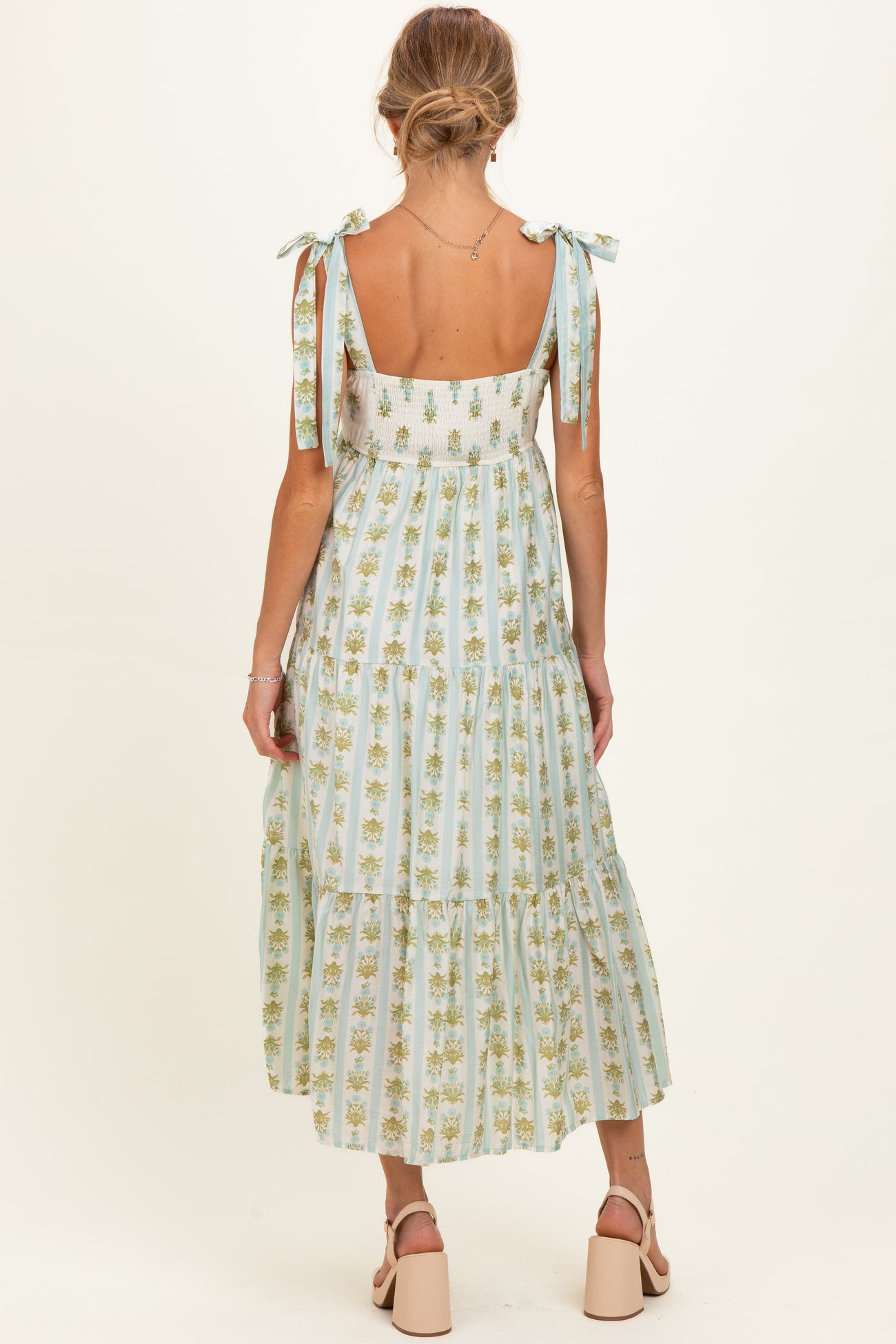 woman wearing a light blue maternity dress with floral print and tie shoulder straps, showcasing a flowing tiered design