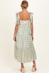 woman wearing a light blue maternity dress with floral print and tie shoulder straps, showcasing a flowing tiered design
