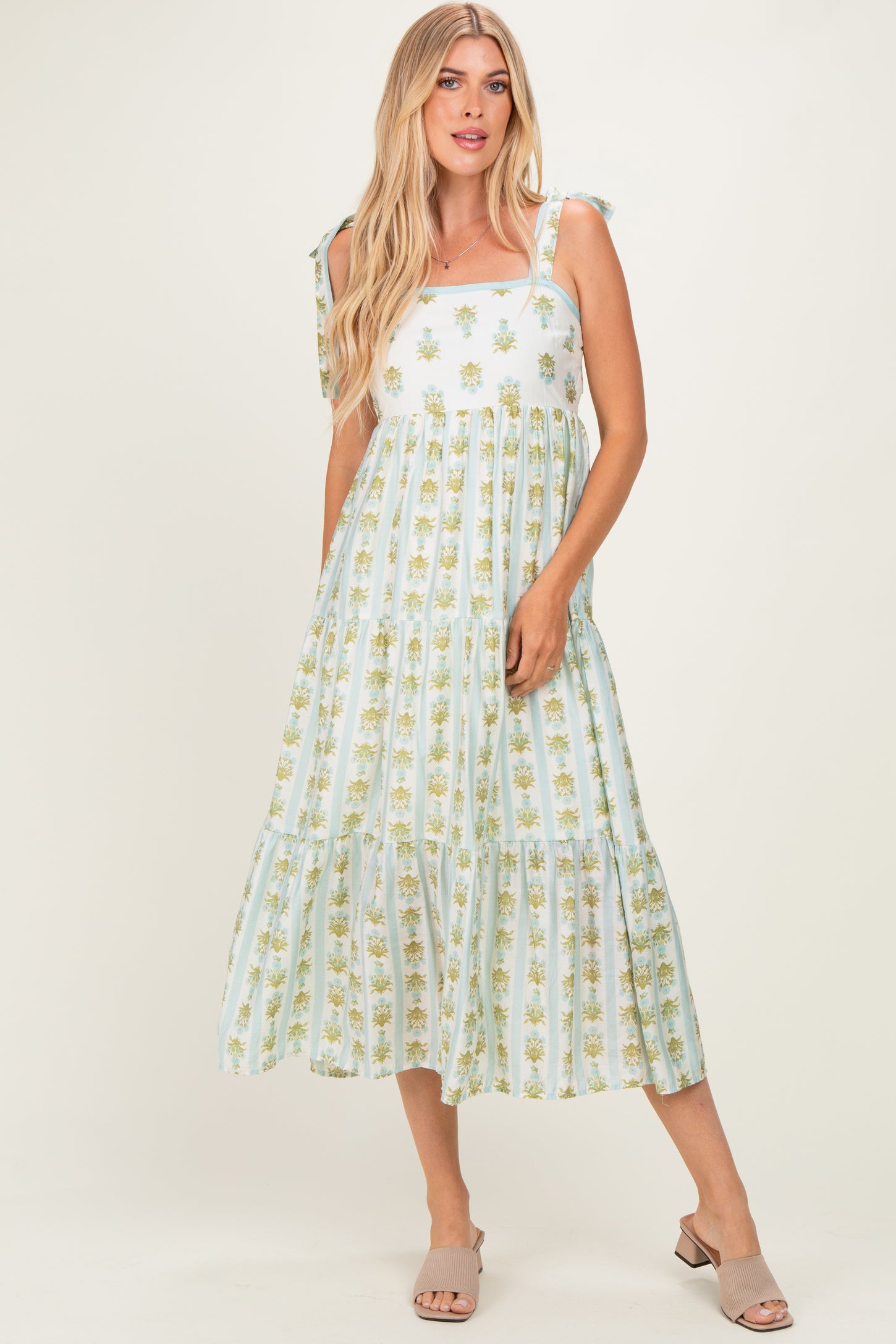 woman wearing a light blue floral print sleeveless maxi dress with tie straps and a tiered skirt