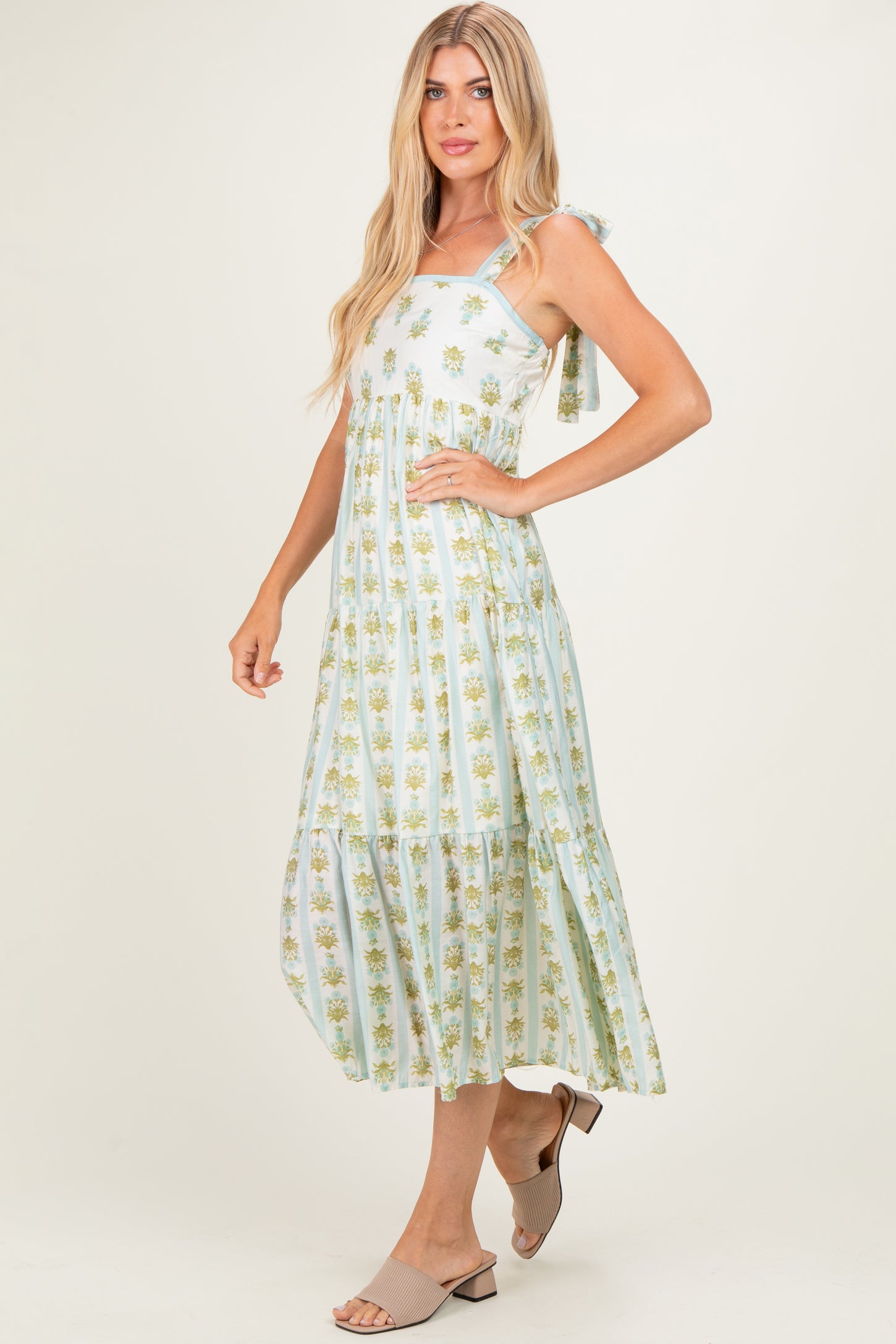 woman wearing a light blue floral maxi dress with tie straps and a tiered design, standing and smiling