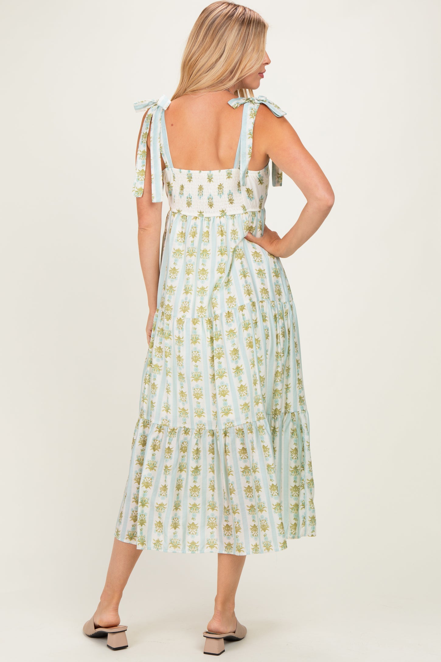 woman wearing a light blue floral maxi dress with tie straps and a tiered skirt, standing with her back facing the camera
