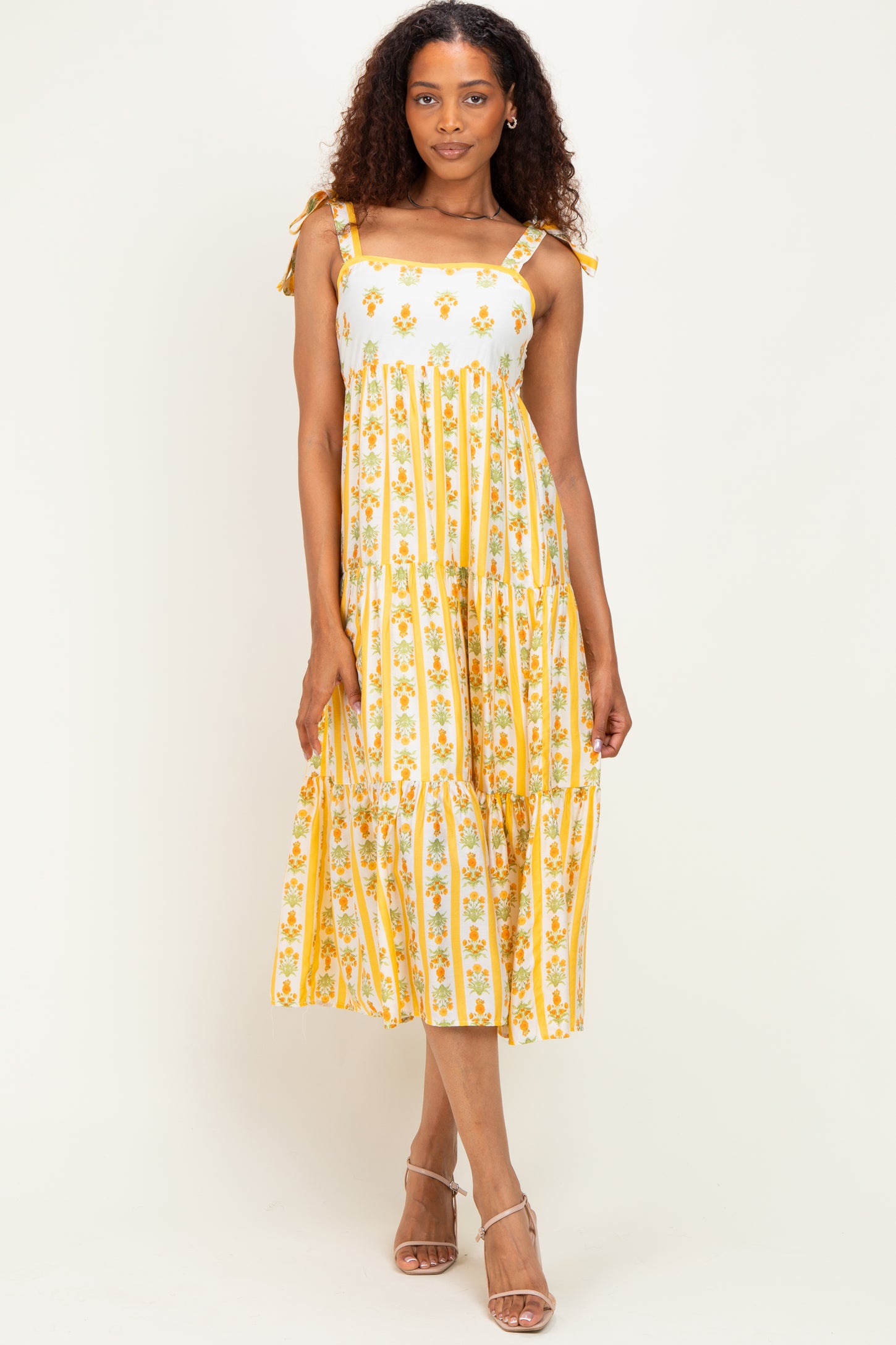 woman wearing a floral yellow and white midi dress with shoulder ties and a tiered design