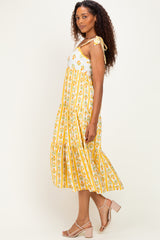 woman wearing a yellow floral print midi dress with striped design and tie shoulder straps