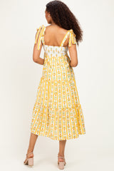 woman wearing a yellow floral tiered midi dress with tie straps and a fitted bodice, showing the back view
