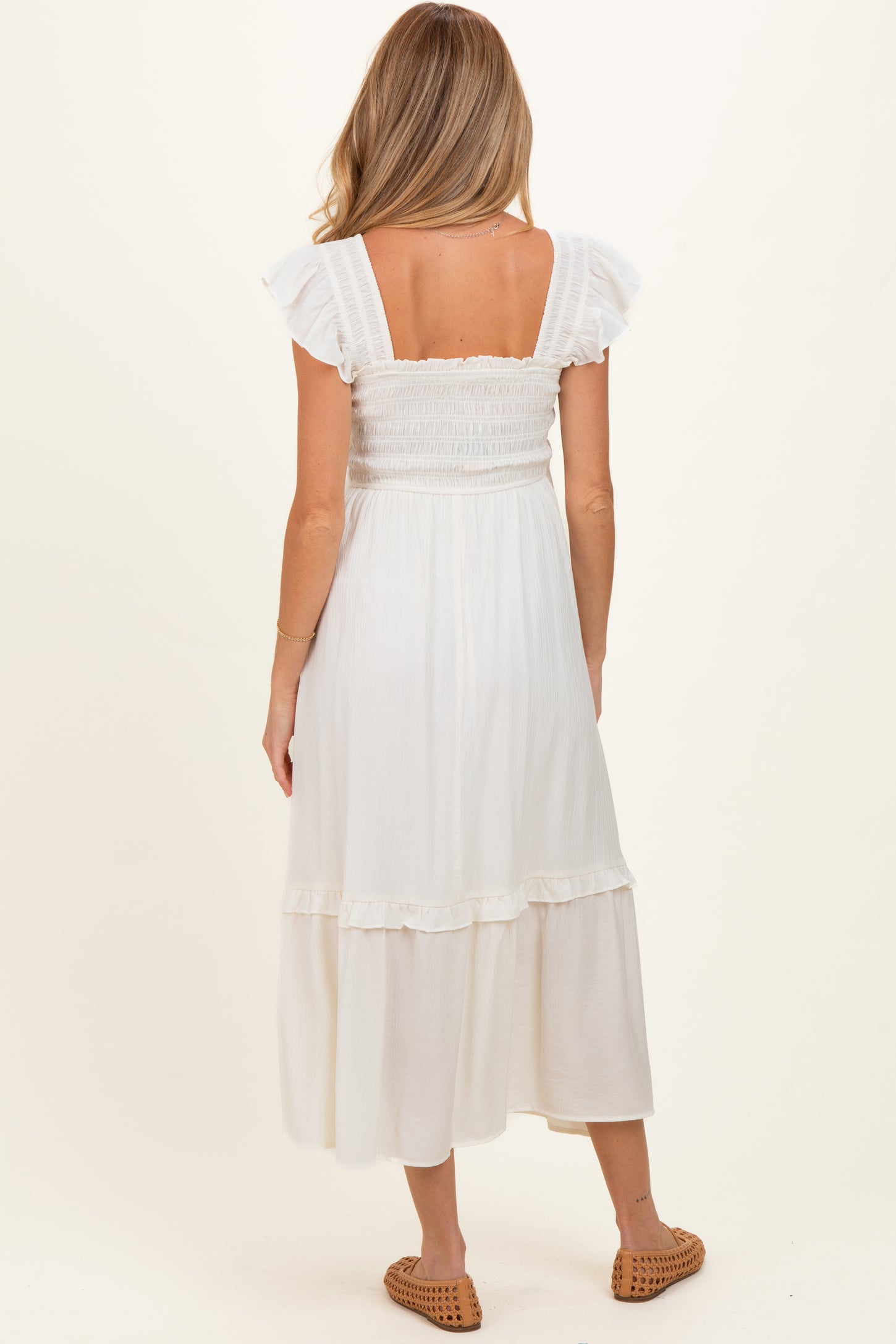 woman wearing a white maternity dress with ruffled sleeves and a tiered skirt seen from the back