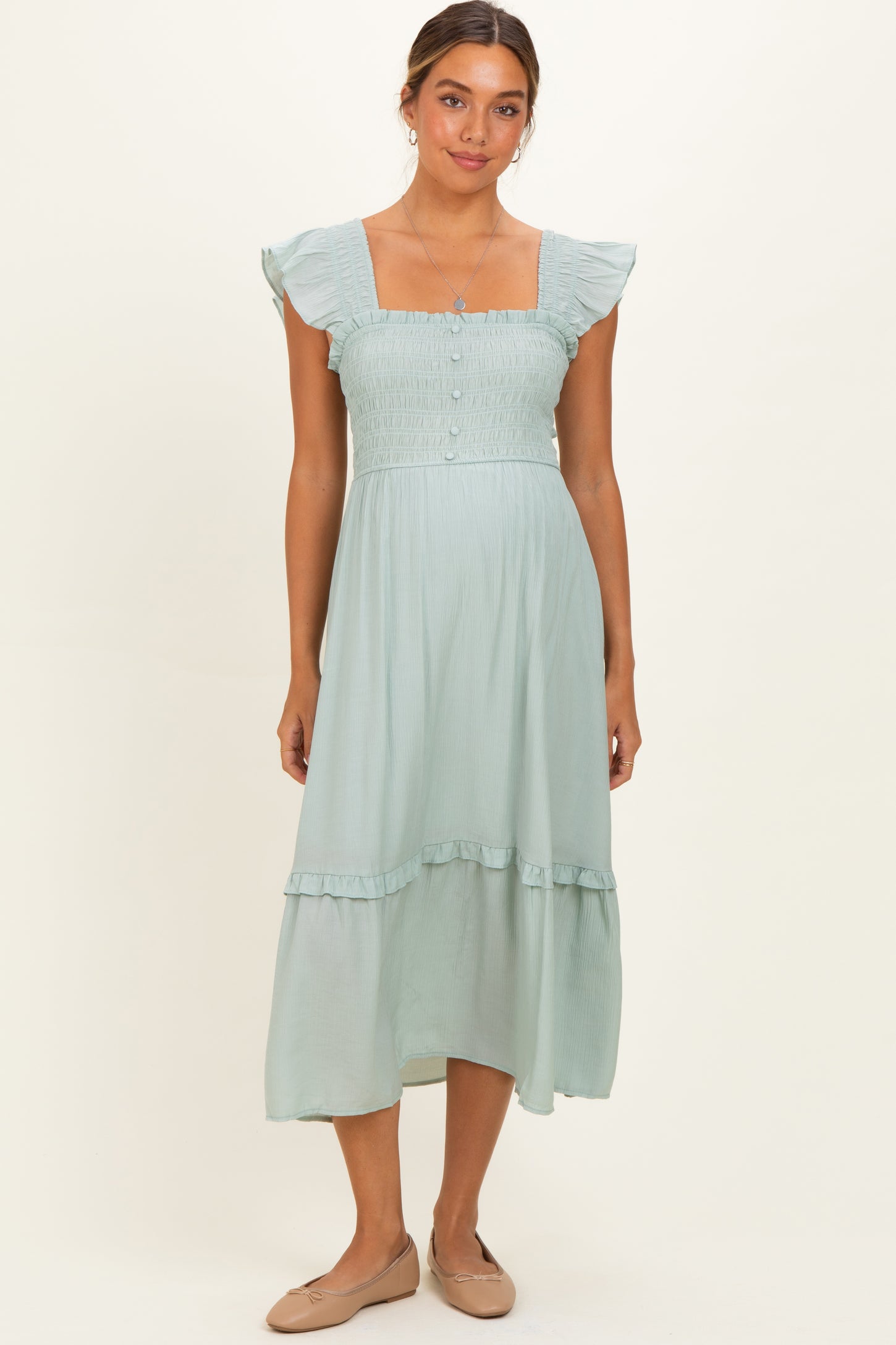 woman wearing a light green maternity dress with ruffle sleeves and a tiered hemline