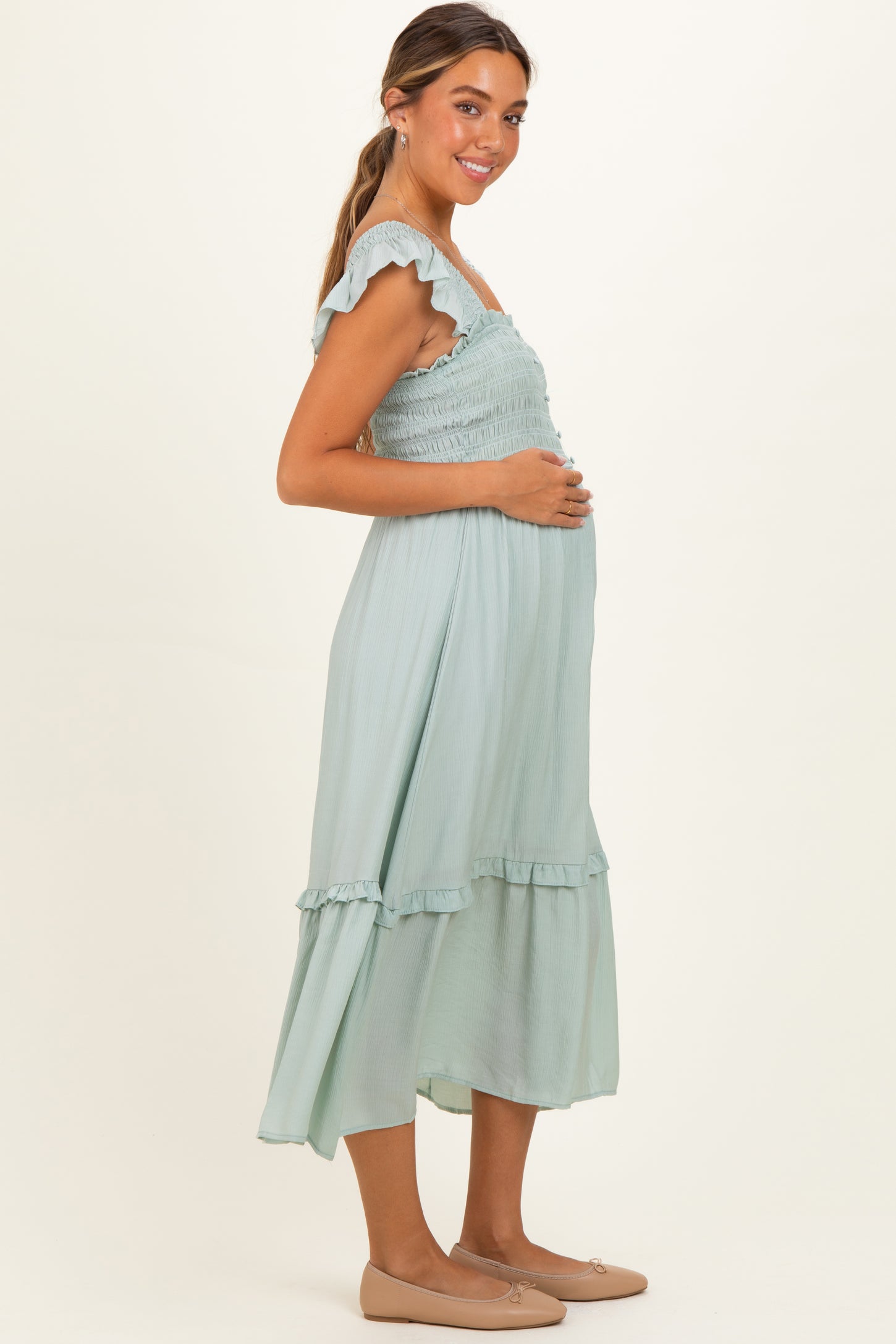 woman wearing a mint green maternity dress with ruffle details and a baby bump visible, posing sideways