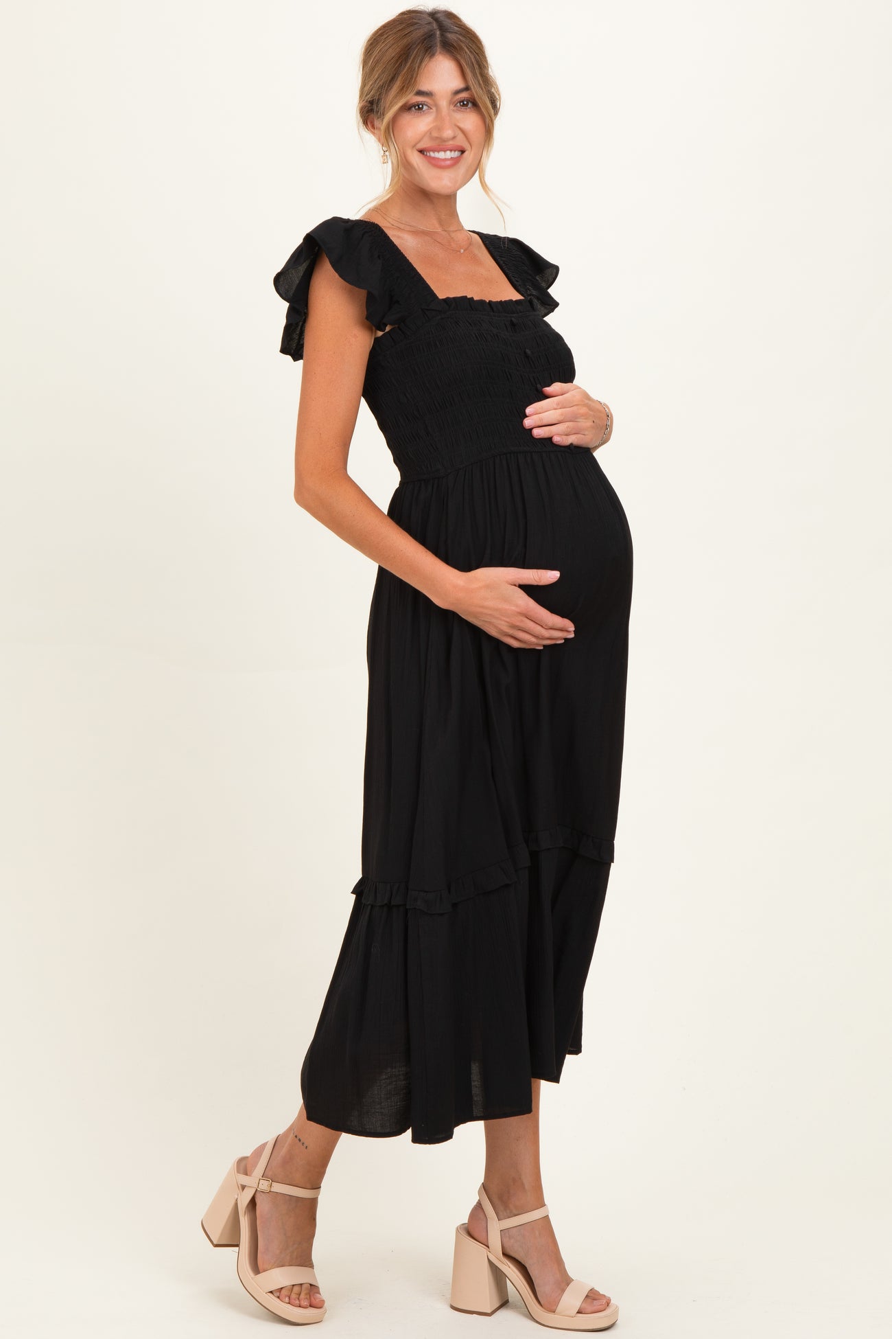 woman wearing a black maternity dress with ruffle sleeves and a smocked bodice, holding her baby bump