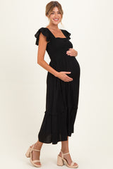 woman wearing a black maternity dress with ruffle sleeves and a smocked bodice, holding her baby bump