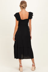 woman wearing a black maternity dress with ruffle sleeves and a tiered skirt, showing her baby bump from the back