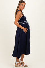 woman wearing a navy blue maternity dress with a tie waist and frill neckline, gently holding her baby bump