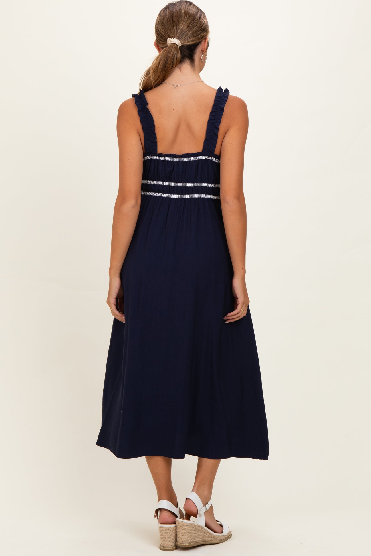 woman wearing a navy blue maternity dress with ruffled straps and back detailing, showing a relaxed fit