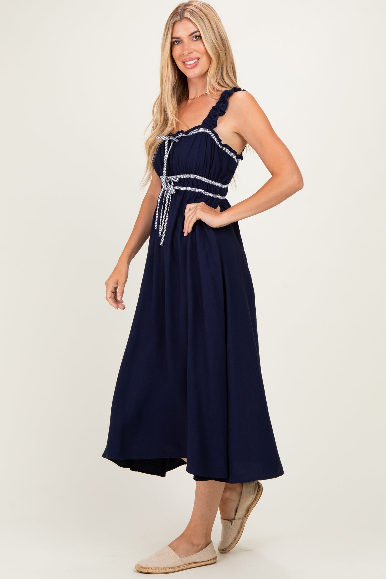 woman wearing a navy blue maxi dress with ruffled straps and a tied waist, standing with a smile